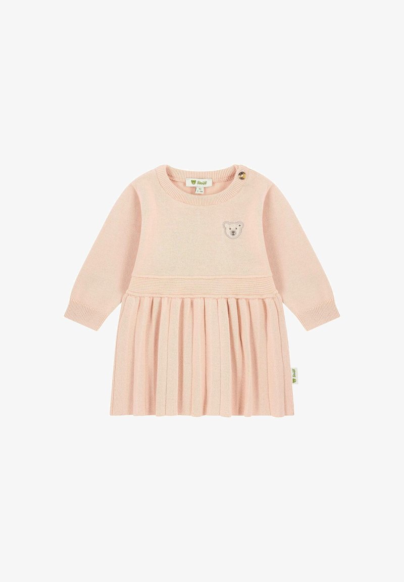 Abito a maglia rosa chiaro con maniche lunghe, gonna plissettata e una toppa a forma di faccia d'orso sul petto. Dotato di chiusura con bottone sulla spalla.