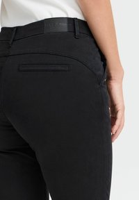 Melni bikses ar gludu tekstūru, kas aprīkotas ar aizmugurējo kabatu un ādas birku ar uzrakstu "PULZ JEANS". Šauras piegriezuma bikses ar pielāgotu dizainu.