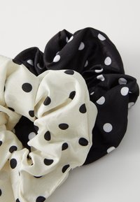 Due scrunchies: uno crema con pois neri e uno nero con pois bianchi, realizzati in tessuto morbido, con un design arricciato e testurizzato.