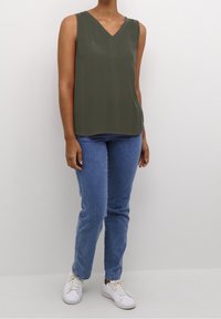 Haut sans manches vert olive avec un col en V, fabriqué en tissu lisse. Associé à un jean bleu clair et des baskets blanches.