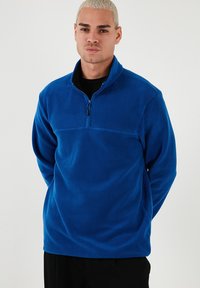 Blauer Fleece-Pullover mit einem Halbreißverschluss an der Vorderseite, der eine einfarbige Textur, lange Ärmel und ein kontrastierendes Oberteil aufweist. Schlichtes und funktionales Design.