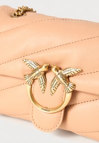 Saco de mão em pele pêssego com design acolchoado, apresentando um detalhe em formato de pássaro em dourado e fecho circular, da marca "Pinko."