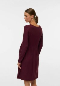 Robe bourgogne à manches longues en tissu côtelé, forme évasée, avec un col rond et une taille froncée pour une silhouette fluide.