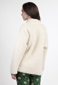 Sudadera de forro polar color crema con cuello alto y superficie texturizada y suave. Presenta un corte holgado y mangas largas.