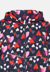 Veste marine avec un motif de cœurs en rouge, rose et crème. Comprend une fermeture éclair à l'avant et une capuche avec un bord élastique. Texture lisse.