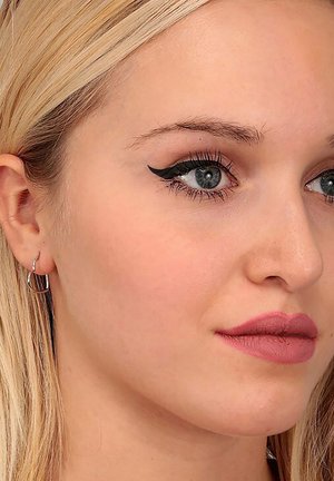 Primo piano di un volto con capelli biondo chiaro, eyeliner a catena audace, labbra piene di un rosa tenue e orecchini a cerchio in argento.