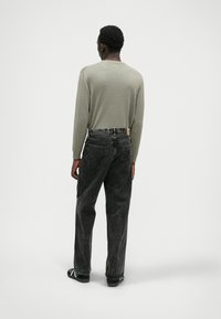 Zeleni dolg rokav, sproščenega kroja, v kombinaciji s širokimi temno sivimi kavbojkami z vidnimi zadnjimi žepi in črnim obutvijo.