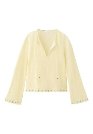 Blusa de manga larga color amarillo claro con escote en V, ajuste holgado y pequeños adornos metálicos a lo largo de los puños y el dobladillo.