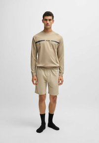 Beige long-sleeve shirt with "BOSS" logo and black stripes, paired with beige shorts. Black knee-length socks complete the outfit.