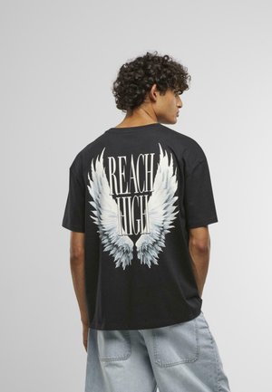 Schwarzes Baumwoll-T-Shirt mit weißem Engelsschwingen-Design und dem Text "REACH HIGH" auf der Rückseite; lockere Passform, kurze Ärmel und Rundhalsausschnitt.