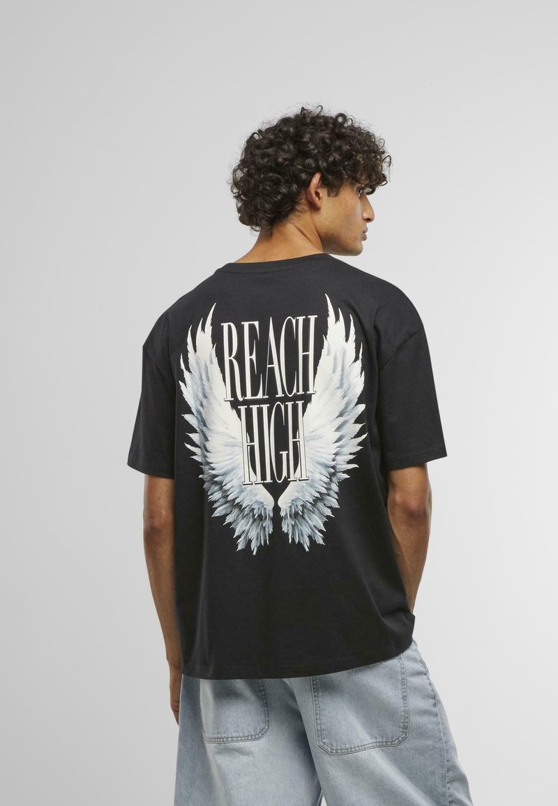 Black cotton t-shirt featuring white angel wing graphic and "REACH HIGH" text on the back; relaxed fit, short sleeves, and crew neck.