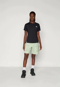 Fekete, rövid ujjú póló, amelyen logó található a mellen, világoszöld cargo rövidnadrággal párosítva, amely több zsebbel és laza szabással rendelkezik.