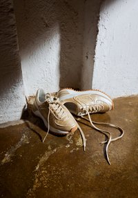 Zapatillas de cuero beige con punta redondeada, cordones planos, lengüeta acolchada y suela de goma con acentos texturizados y talón blanco contrastante.