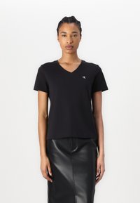 T-shirt nera in cotone con scollo a V, maniche corte e un piccolo logo bianco sul petto. Tessuto strutturato, design aderente.