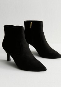 Stivaletti neri in suede con punta affilata, tacco sottile e dettagli con zip laterale. Texture liscia con un design aderente alla caviglia.