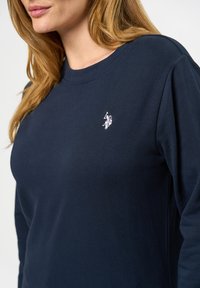 Námořnická modrá pánská dlouhý rukáv tričko vyrobené z bavlny, s malým bílým logem na hrudi a kulatým výstřihem s hladkým povrchem.