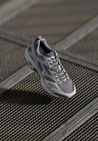 Pantofii atletici gri cu un superior din plasă și material sintetic, guler căptușit, șireturi și talpă texturată, prezentând o marcă subtilă și un design ușor.