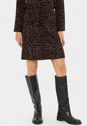 Bruine en zwarte luipaardprint rok gecombineerd met kniehoge zwarte leren laarzen bij een model dat voor een witte achtergrond staat.
