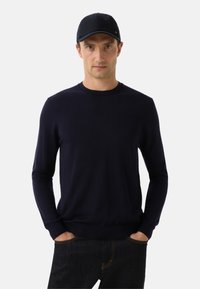 Námořnická modrá dlouhá svetr z měkké pleteniny, doplněný odpovídající čepicí. Úzký střih, kulatý výstřih a ribbované manžety.