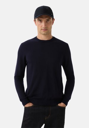 Mørkeblå langærmet sweater lavet af blødt strikket stof, parret med en matchende kasket. Tætsiddende pasform, rund halsudskæring og ribbede manchetter.