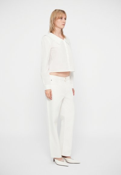 Chemise blanche cintrée avec un large col, assortie à un jean blanc taille haute aux jambes droites. Des escarpins blancs à bout pointu complètent le look.