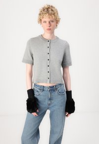 Graue, kurze Strickjacke mit kurzen Ärmeln und rundem Ausschnitt, mit einer vorderen Knopfleiste. Kombiniert mit hoch taillierten blauen Jeans und schwarzen fingerlosen Handschuhen.