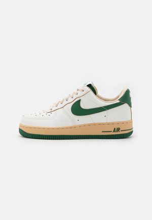 Hvide lædersneakers med grønne accenter, tan mellemsål, perforeret tå og "AIR" branding i grønt på siden. Flade snørebånd i beige.