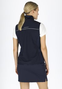 Gilet senza maniche navy realizzato in materiale leggero, caratterizzato da dettagli in argento e un colletto alto, abbinato a una gonna navy coordinata.