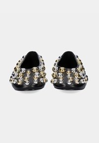 Zapatos planos negros con tachuelas redondas metálicas en plata y dorado, distribuidas uniformemente por toda la superficie, con un acabado elegante y suave.