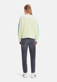 Knit sweater with yellow and blue stripes, relaxed fit, paired with dark gray jeans and white sneakers featuring neon accents.