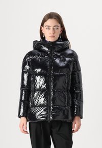 Chaqueta acolchada negra brillante con capucha, que cuenta con cierre de cremallera y secciones acolchadas. Incluye bolsillos laterales y un pequeño parche de logo.
