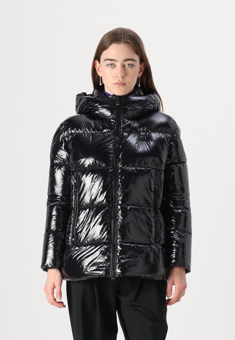 Chaqueta acolchada negra brillante con capucha, que cuenta con cierre de cremallera y secciones acolchadas. Incluye bolsillos laterales y un pequeño parche de logo.