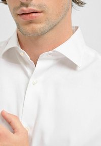 Vit skjorta med spridd krage och en slät yta, med pärlemorska knappar och subtila sömmar vid knäppningen.