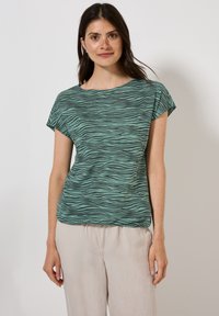 Grön och svart randig t-shirt med korta ärmar och vid halsringning. Lätt tyg med en mjuk textur, kombinerat med ljusa, lösa byxor.
