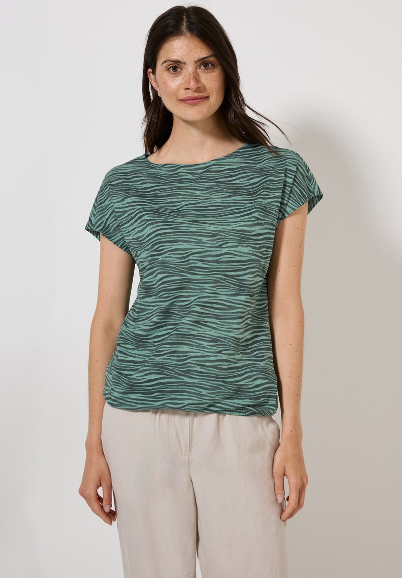 Grön och svart randig t-shirt med korta ärmar och vid halsringning. Lätt tyg med en mjuk textur, kombinerat med ljusa, lösa byxor.