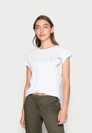 Witte katoenen t-shirt met opgerolde mouwen, voorzien van een zwarte hartcontour en tekstontwerp aan de linkerkant. Gecombineerd met olijfgroene broeken.
