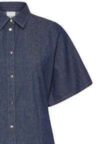 Chemise en denim bleu foncé à manches courtes, boutons-pression métalliques, col pointu et coutures visibles. Seule la moitié supérieure est visible.