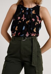Top senza maniche nero con un motivo colorato di farfalle; abbinato a pantaloni cargo verde oliva con cintura e tasche laterali.