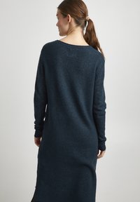 Pull en tricot bleu marine long avec une coupe décontractée, des poignets côtelés et des fentes sur les côtés, présentant un tissu texturé et doux.