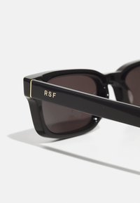 Black rectangular sunglasses with dark lenses, featuring a glossy finish and gold accents. "RSF" is printed on the sides.