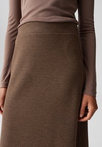 Gonna marrone, con texture, a vita alta, caratterizzata da un design liscio e dettagli di cucitura sottili. Maglia a maniche lunghe in una tonalità tenue.