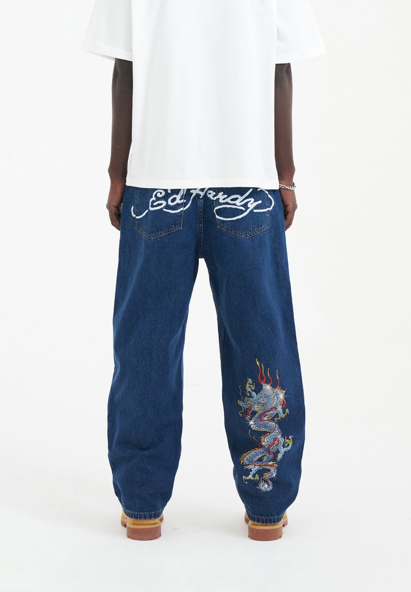 Modré džínové kalhoty mají na levé noze velký vyšívaný motiv draka v mnoha barvách. Na zadní straně je bílý šev, na kterém je napsáno "Ed Hardy".