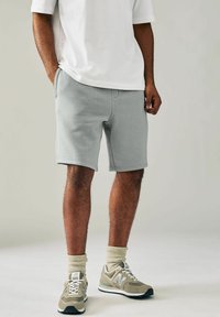 Bermudas de mezcla de algodón gris claro para hombre con bolsillos laterales, diseño liso y corte relajado, combinadas con zapatillas beige y calcetines de canalé.