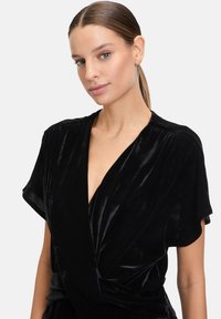 Schwarzes Samt-Wickeltop mit kurzen Ärmeln, tiefem V-Ausschnitt und gerafften Details. Glatte Textur mit tailliertem Design.