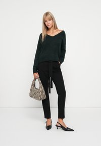 Donkergroene gebreide trui met V-hals, zwarte tapered broek met strik taille, zwarte slingback hakken en een handtas met textuur in slangenprint.