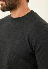 Dunkelgrauer Strickpullover mit Rundkragen. Besitzt ein dezentes Logo auf der Brust und einen weichen, strukturierten Stoff.