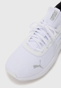 White athletic shoe with mesh upper, flat white laces, and gray Puma logo. Features a cushioned sole and sleek, modern design.