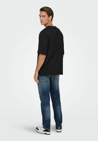 Schwarzes übergroßes T-Shirt mit kurzen Ärmeln, kombiniert mit blauen Denim-Jeans. Das Outfit wird durch schwarz-weiße Sportschuhe komplettiert.
