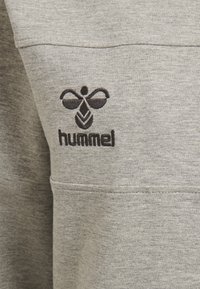 Grå sweatshirt med en svart broderad logotyp som har en stiliserad geting och ordet "hummel" nedanför. Mjuk textur och avslappnad design.