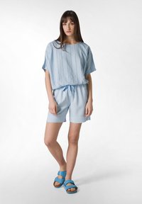 Ljusblå kortärmad topp med vertikala ränder, tillsammans med matchande shorts. Sandalerna har dubbla spännen och en plattformssula.